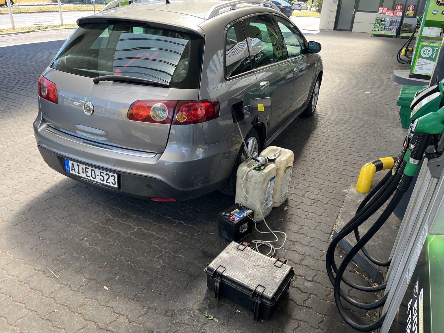 Üzemanyag lefejtése egy szürke autóból a benzinkúton